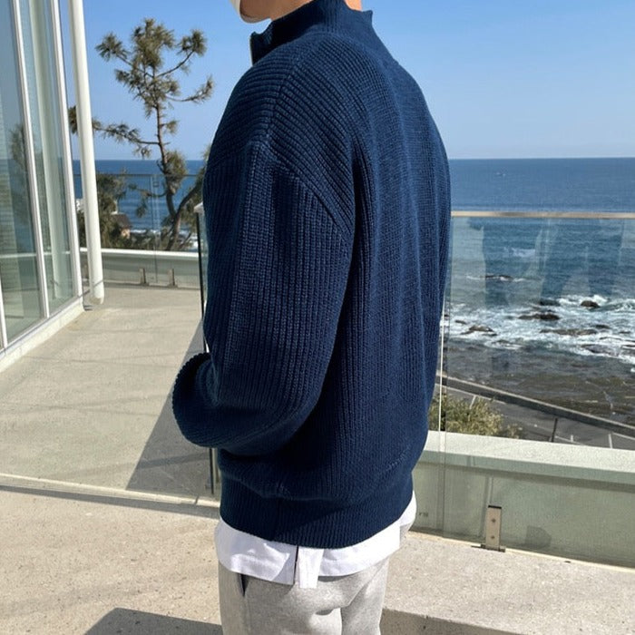 Uomo con maglione blu scuro in lana, vista mare. Moda maschile autunnale, abbigliamento casual elegante, sfondo costiero.