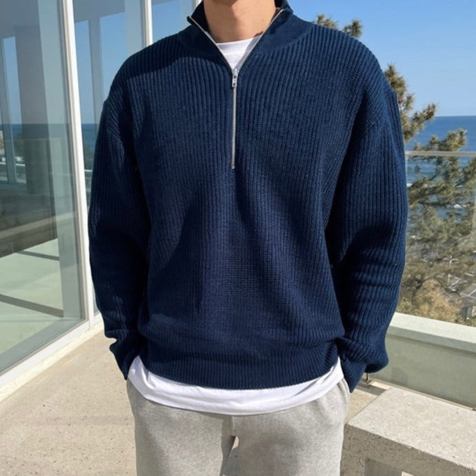 Maglione blu a collo alto con zip, indossato da uomo su terrazza con vista mare. Moda casual maschile, abbigliamento autunnale, stile moderno.