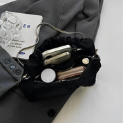 Borsa a tracolla nera in raso con catena argento, contenente smartphone, portafoglio e accessori, su giacca grigia. Elegante e pratica.
