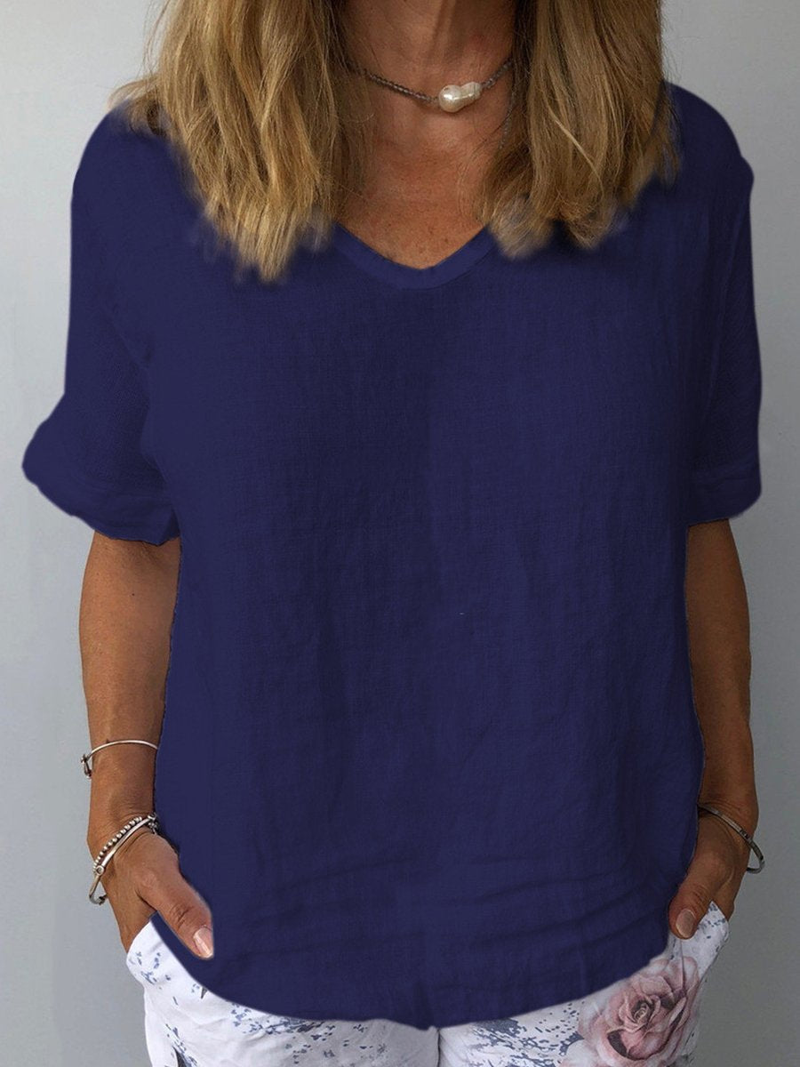 Donna con maglietta blu scuro in lino, scollo a V, maniche corte, abbinata a pantaloni bianchi con stampa floreale. Moda casual estiva.
