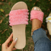 Sandali donna rosa con frange, suola intrecciata beige, indossati su prato verde. Moda estiva, calzature casual eleganti.