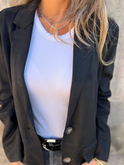 Donna con giacca nera elegante, maglietta bianca e collana d'argento. Moda femminile, abbigliamento casual chic, stile contemporaneo.