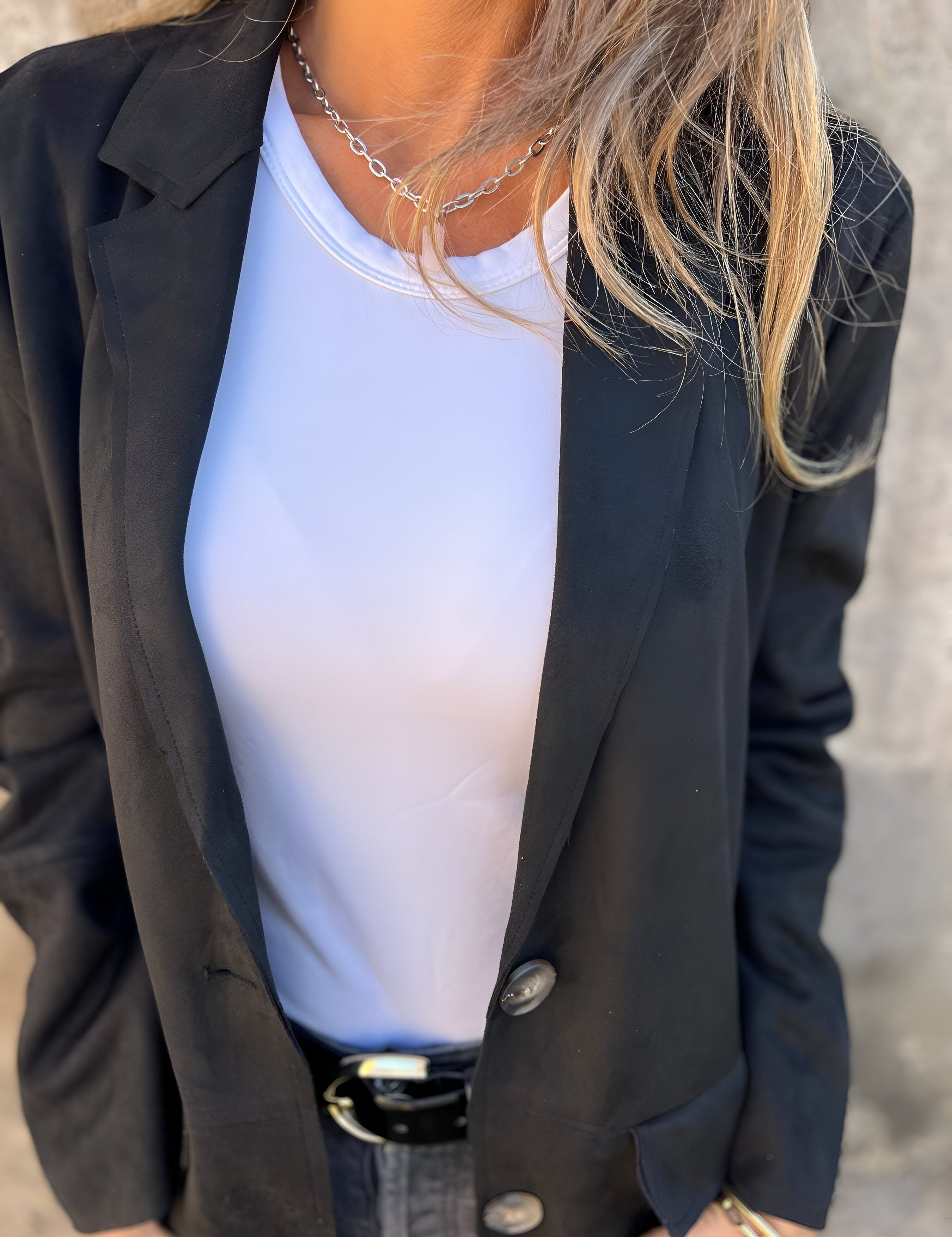 Donna con giacca nera elegante, maglietta bianca e collana d'argento. Moda femminile, abbigliamento casual chic, stile contemporaneo.