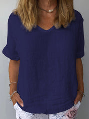 Donna con maglietta blu scuro in lino, scollo a V, maniche corte, abbinata a pantaloni bianchi con stampa floreale. Moda estiva casual elegante.