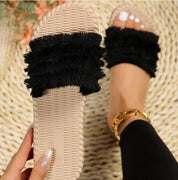 Sandali estivi da donna con suola intrecciata beige e fascia nera in tessuto frangiato, indossati su tappeto chiaro. Accessorio moda casual.