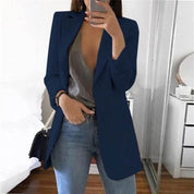 Donna con blazer blu, top grigio scollato e jeans, specchio sullo sfondo. Moda casual elegante, abbigliamento femminile trendy.