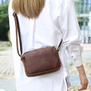 Donna con borsa a tracolla in pelle marrone, indossa camicia bianca. Accessorio moda elegante, ideale per look casual e urbano.