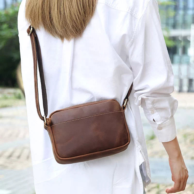 Donna con borsa a tracolla in pelle marrone, indossa camicia bianca. Accessorio moda elegante, ideale per look casual e urbano.