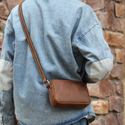 Giacca di jeans uomo con borsa a tracolla in pelle marrone, moda casual, sfondo in pietra. Accessorio elegante e pratico per ogni occasione.