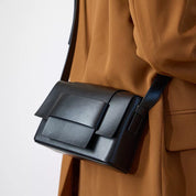 Borsa a tracolla in pelle nera elegante su cappotto marrone, design moderno e minimalista, accessorio moda donna, stile autunno inverno.