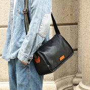 Uomo con giacca di jeans e borsa a tracolla in pelle nera, dettaglio etichetta marrone, moda casual urbana, accessorio maschile elegante.