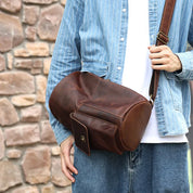 Uomo con borsa a tracolla in pelle marrone, indossa camicia a righe blu e jeans. Accessorio moda maschile, stile casual, sfondo in pietra.