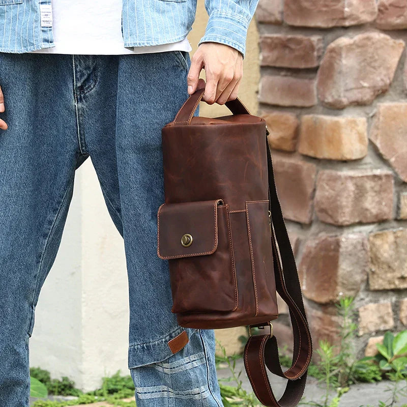 Borsa a tracolla in pelle marrone per uomo, design vintage, con tasca frontale e manico, indossata con jeans casual. Accessorio moda maschile.