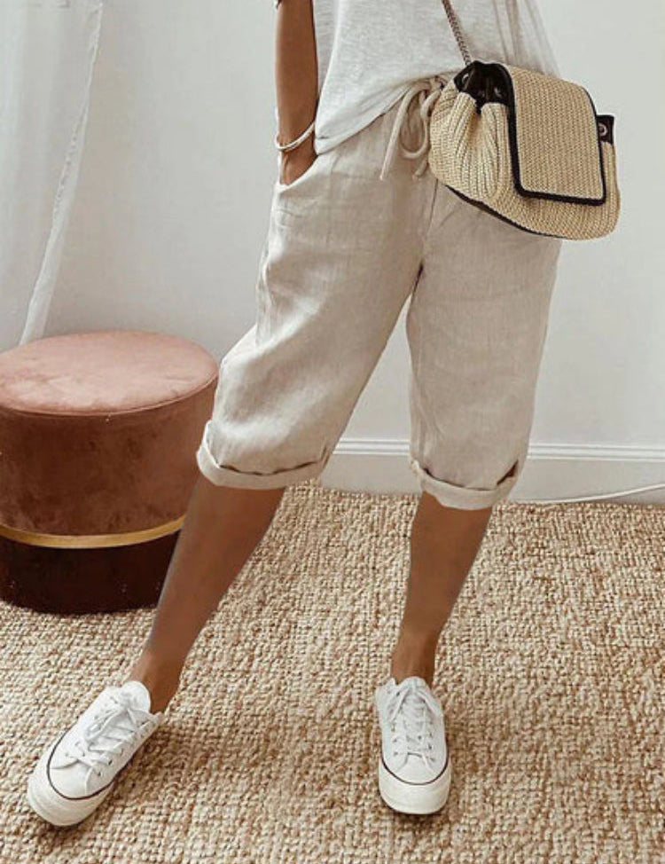 Pantaloncini beige in lino, stile casual, abbinati a sneakers bianche e borsa a tracolla intrecciata. Outfit estivo donna, moda comoda.