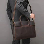 Uomo in abito grigio con borsa a tracolla in pelle marrone, elegante e professionale, ideale per lavoro e ufficio. Accessorio moda maschile.