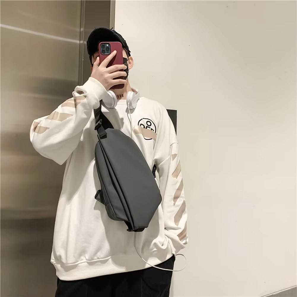 Uomo con felpa bianca oversize, cappello nero e borsa a tracolla grigia, scatta selfie con smartphone rosso. Stile casual moderno.