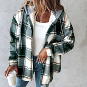 Donna con camicia a quadri verde e bianca, cappuccio grigio, jeans strappati, tiene una tazza di caffè. Moda casual autunnale.