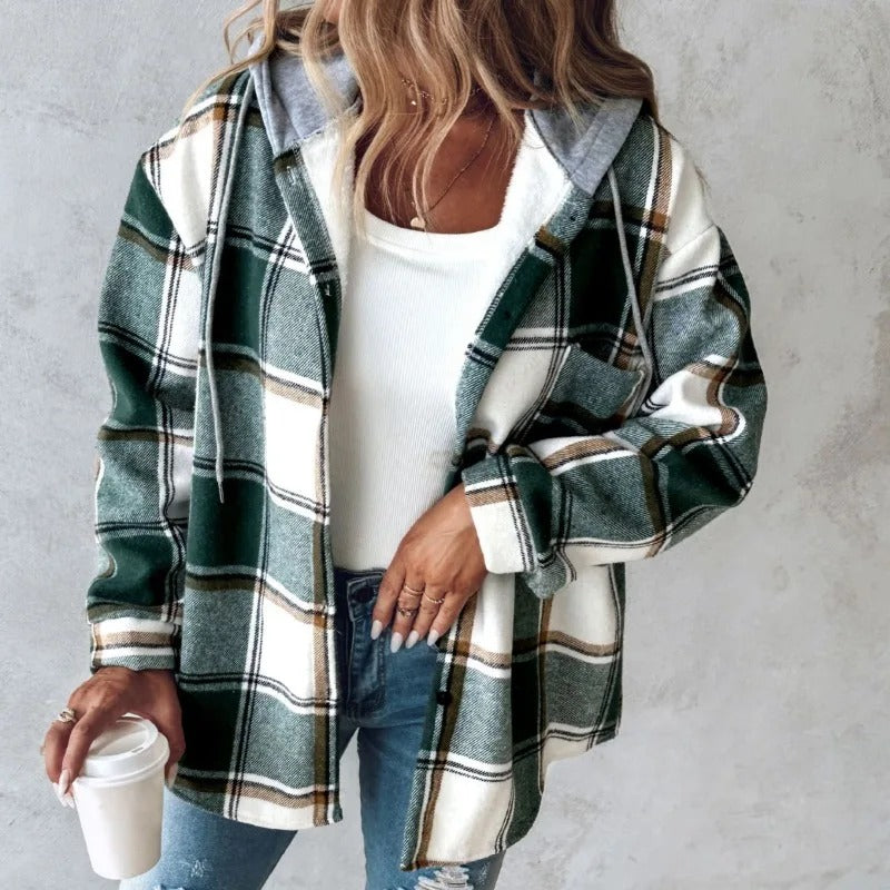Donna con camicia a quadri verde e bianca, cappuccio grigio, jeans strappati, tiene una tazza di caffè. Moda casual autunnale.