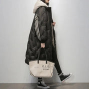 Cappotto lungo nero trapuntato con cappuccio, dettagli a righe bianche, abbinato a borsa beige e sneakers nere. Moda invernale casual donna.