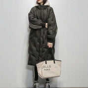 Donna con cappotto lungo nero trapuntato, dettagli a righe bianche, e borsa beige "Céllo Paris". Stile invernale, moda urbana, abbigliamento casual.