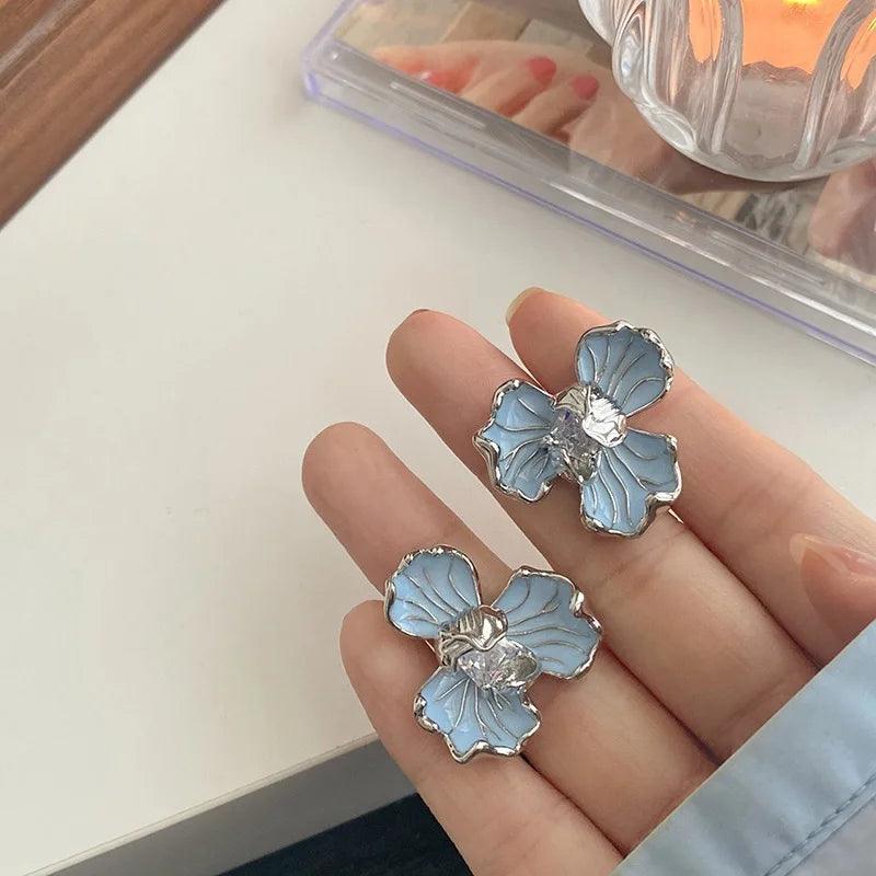 Orecchini a forma di fiore blu con dettagli argentati su sfondo bianco. Accessori moda eleganti, gioielli femminili, stile floreale.