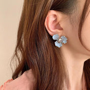 Orecchino a forma di fiore blu su donna, accessorio moda elegante, gioiello femminile, dettaglio capelli castani, stile raffinato.