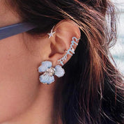 Orecchino a forma di fiore blu con dettaglio centrale brillante su orecchio femminile, accompagnato da piercing a stella e scritta "dream".