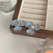 Orecchini a forma di fiore blu con dettagli argentati su vassoio di legno, design elegante, accessori moda donna, gioielli floreali.