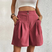 Donna con pantaloncini rosa a vita alta, tasche laterali, bottoni decorativi, indossa top bianco. Moda estiva casual, abbigliamento femminile trendy.