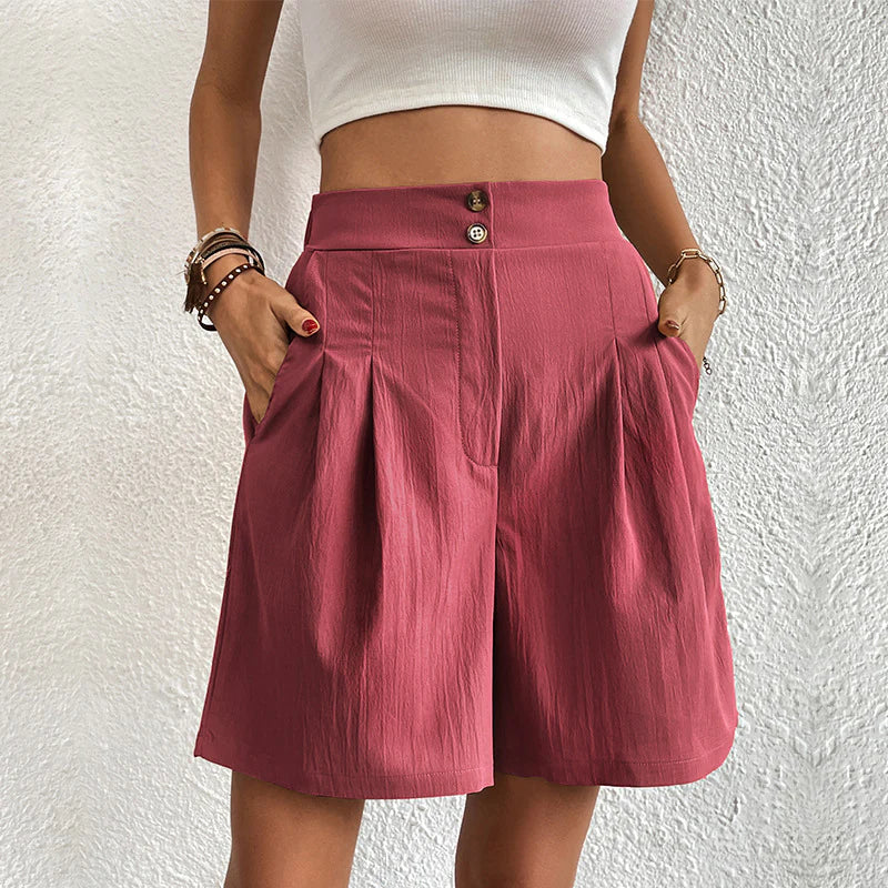 Donna con pantaloncini rosa a vita alta, tasche laterali, bottoni decorativi, indossa top bianco. Moda estiva casual, abbigliamento femminile trendy.