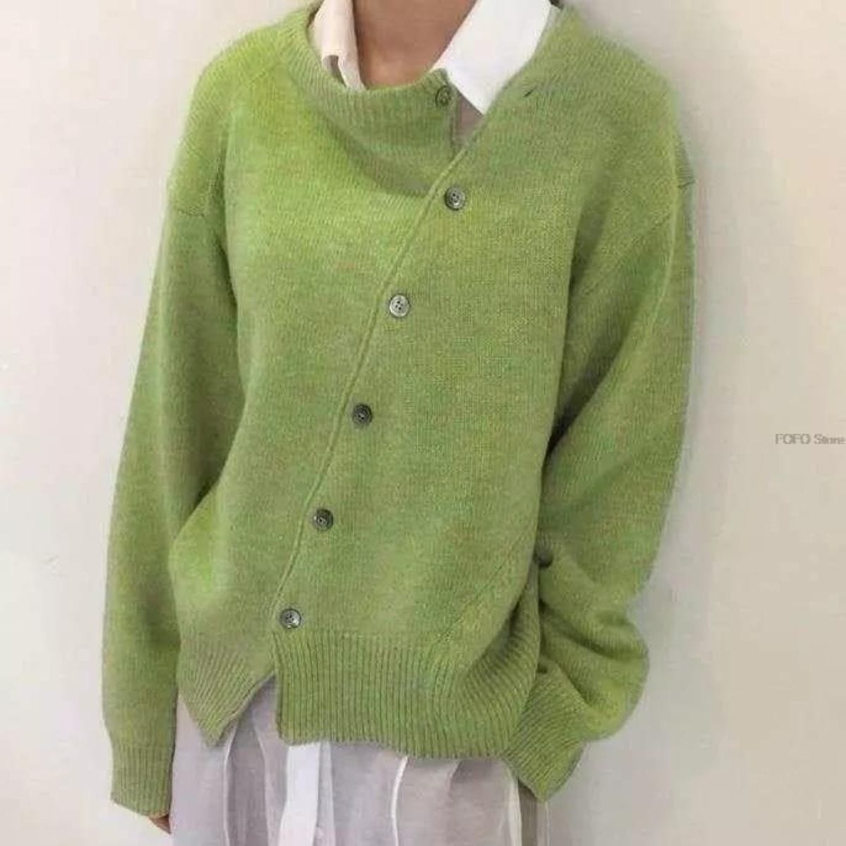 Maglione verde chiaro asimmetrico con bottoni, indossato sopra camicia bianca. Moda donna, abbigliamento casual elegante, tendenza autunno.