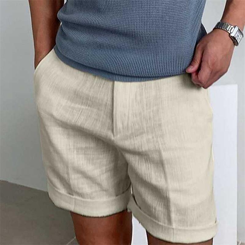 Uomo con pantaloncini beige in lino, mani in tasca, indossa maglietta blu e orologio. Moda estiva casual, abbigliamento maschile elegante.