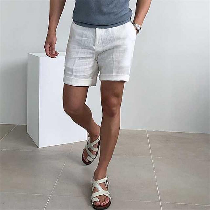 Uomo in pantaloncini bianchi di lino, maglietta grigia e sandali bianchi. Moda estiva casual, abbigliamento leggero e traspirante.