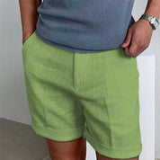 Uomo con pantaloncini verdi casual, maglietta grigia a maniche corte, orologio al polso. Moda estiva maschile, abbigliamento leggero e comodo.