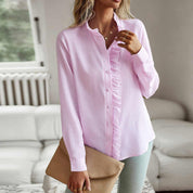 Camicia rosa a righe con volant, indossata da donna in salotto moderno, abbinata a pantaloni chiari e borsa beige. Moda casual elegante.