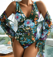 Costume intero floreale verde con scollo a V, abbinato a copricostume trasparente. Moda mare donna, abbigliamento estivo elegante e colorato.