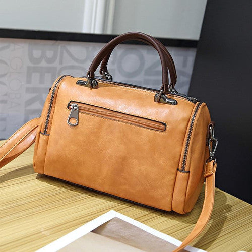 Borsa a mano in pelle marrone chiaro con cerniera, manici scuri e tracolla regolabile su tavolo di legno. Elegante accessorio moda donna.