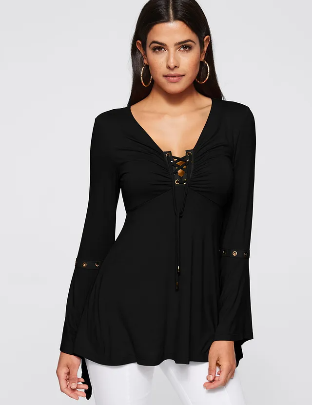 Donna con maglia nera a maniche lunghe, scollo a V con lacci, dettagli metallici, indossa pantaloni bianchi. Moda femminile elegante e casual.