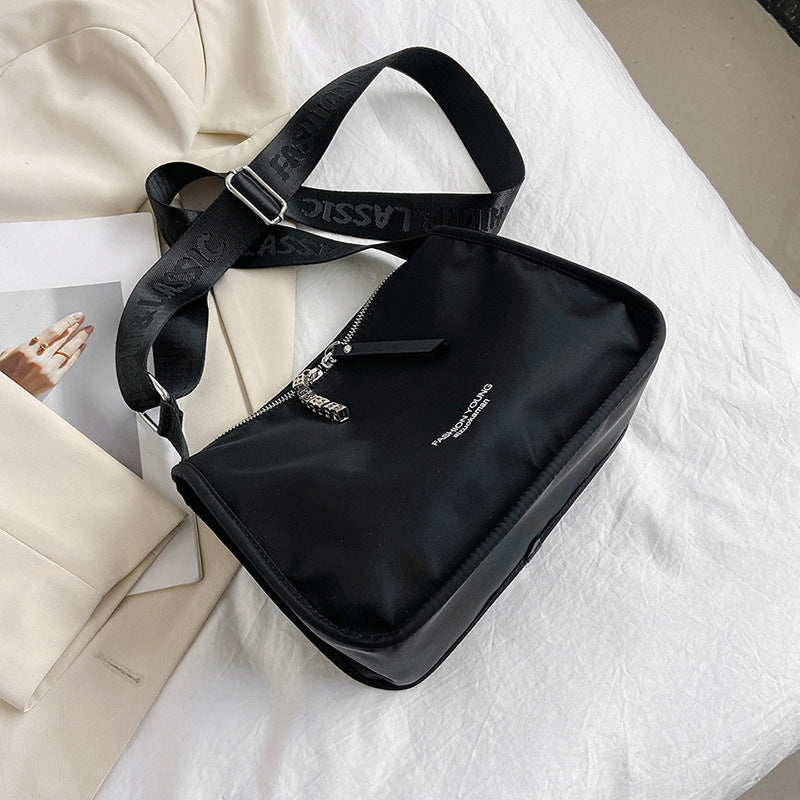 Borsa a tracolla nera in nylon su letto bianco, con cerniera argentata e cinturino regolabile. Design elegante, perfetta per moda casual e urbana.