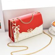Borsa a tracolla elegante rossa e bianca con catena dorata, decorata con ciondolo perle e fiocco. Accessorio moda donna, stile chic e moderno.