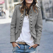 Giacca militare donna grigia, doppio petto, bottoni metallici, stile casual, abbinata a jeans strappati e maglietta bianca. Moda urbana femminile.