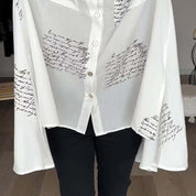 Camicia bianca donna con scritte nere, maniche ampie, bottoni frontali. Moda elegante, tessuto leggero, ideale per look casual e formali.