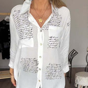 Camicia bianca da donna con scritte nere, maniche lunghe, colletto classico, tasca frontale, abbinata a collana con ciondolo a stella. Moda casual elegante.
