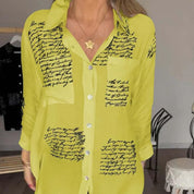 Camicia donna gialla con scritte nere, maniche lunghe, colletto classico, bottoni frontali, stile casual elegante, moda femminile autunno.