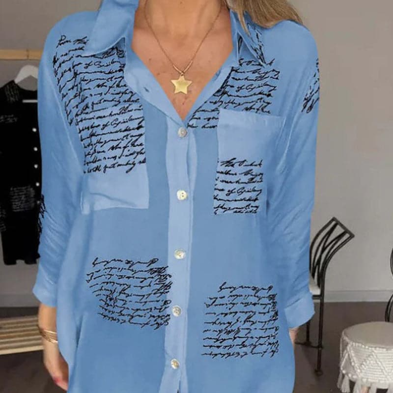 Camicia donna azzurra con scritte nere, maniche lunghe, colletto classico, bottoni frontali. Moda casual elegante, tessuto leggero.