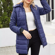 Giacca invernale donna blu, imbottita, con cappuccio, chiusura zip, indossata su top bianco e pantaloni neri. Moda casual, abbigliamento caldo.