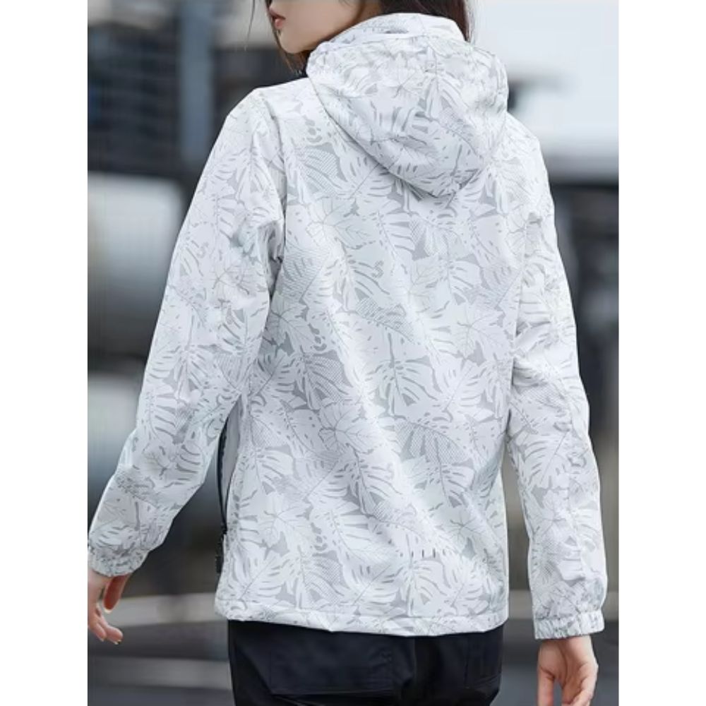 Giacca a vento bianca con cappuccio, motivo foglie, donna di spalle. Abbigliamento outdoor, impermeabile, stile casual, moda autunnale.