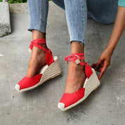 Donna indossa espadrillas rosse con zeppa in corda, lacci alla caviglia, abbinate a jeans. Scarpe estive eleganti, moda casual.