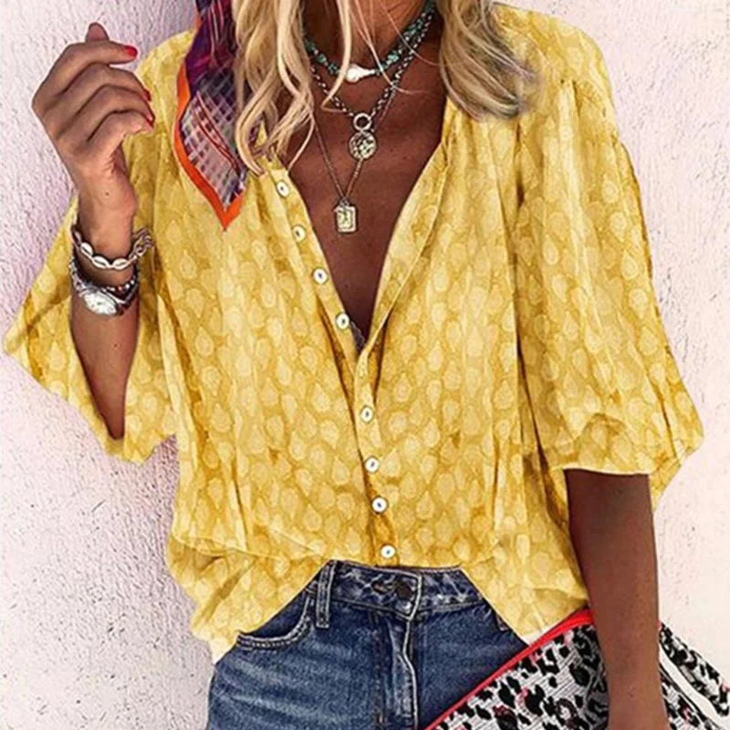 Blusa gialla a maniche corte con motivo a foglie, abbinata a jeans blu. Accessori: collane, bracciali e borsa con stampa animalier. Moda estiva casual.