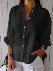 Camicia nera da donna in lino, maniche lunghe, bottoni bianchi, stile casual, abbinata a pantaloni bianchi. Accessori: collane e bracciali dorati.